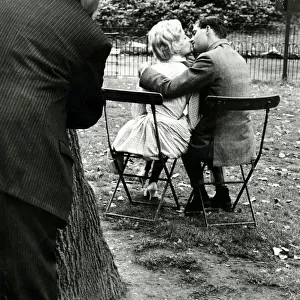 A couple kissing in the park all the while being watched by a dirty old man