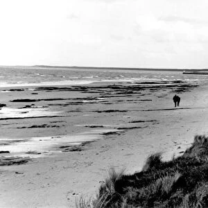 A couple take a stroll along Nairn beach in Scotland. Circa 1970