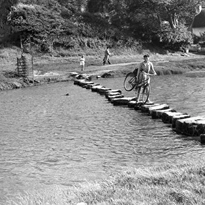 A couple of young women use stepping stones to cross the Ewenny River that rises to