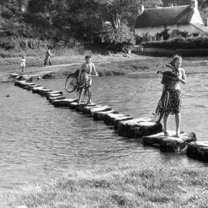 A couple of young women use stepping stones to cross the Ewenny River that rises to