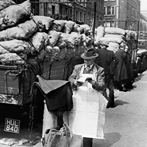 Covent Garden Market stall vendor stops to read a magazine. Circa 1955