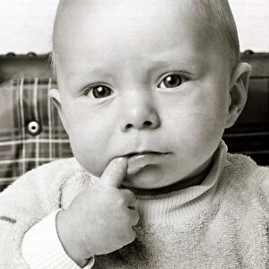 A cute baby looking bemused thinking with one finger in his mouth October 1969