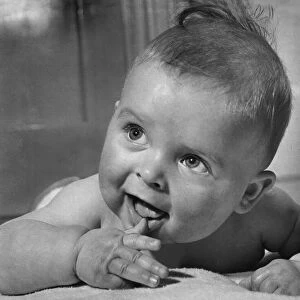 Cute baby sucking on his thumb and smiling February 1959