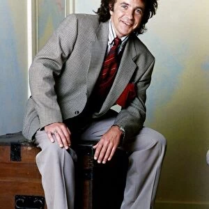 David Essex Singer sitting on a blanket box wearing a suit and yellow socks