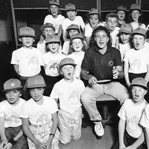 David Essex Singer surrounded by choir of school children wearing baseball caps