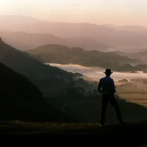Dawn rises over the Lake District as a walker travels along a lakeland pass