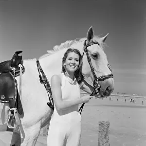 Diana Rigg, who plays Emma Peel, smiling with a white horse on the beach at St Mary