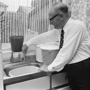 An elderly man running the tap in his kitchen, filling up buckets as a water shortage An elderly man running the tap in his kitchen, filling up buckets as a water shortage