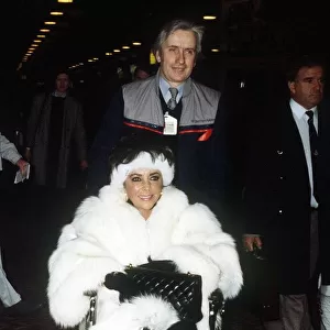 Elizabeth Taylor Jan 1987 wearing White Fur coat in wheelchair at Heathrow Airport