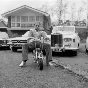 Elton John fotografiado en su hogar, sentado sobre una pequeña motocicleta frente a cuatro de sus.