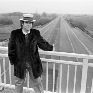 Elton John pictured standing on a bridge over the motorway. 5th December 1982