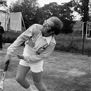 Elton John playing tennis on an outer court at Wimbledon. 25th June 1974
