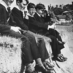 Eton pupils sitting on the edge of river bank of the Thames at Windsor. 1955