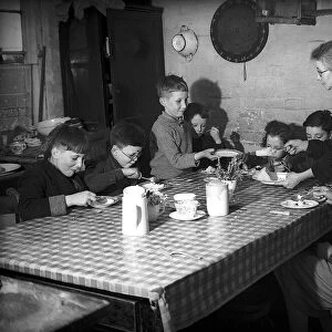 Evacuees with women voluntary service helper sitting at table eating food during WW2