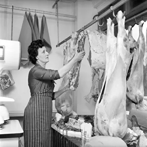 A female butcher seen here at work in her shop, hanging up joints on the rack ready to be