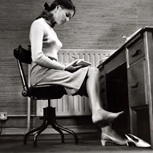 Female office worker sitting taking notes. Writing barefoot / taking shoe