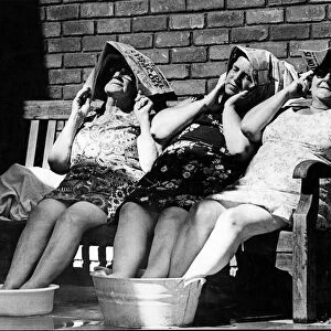 Three female old age pensioners sit out in the sun, cooling their feet in buckets of