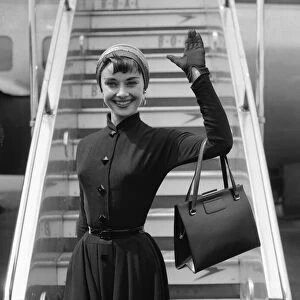 Film actress Audrey Hepburn waves as she stands in front of the steps of her plane at