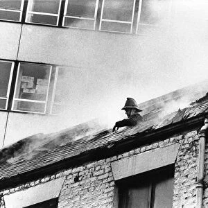 A firefighter pokes his head through the roof of the smoke filled building to grab some
