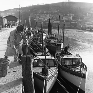 Fisherman ties his boat up in the harbour at Looe, Cornwall. Circa 1953