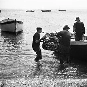 Fishermen loading lobster pots on to a small boat at Cadgwith. July 1939