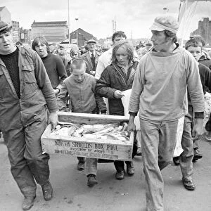 Two fishermen pursued by an eager crowd, bring a box of fish ashore in 1980