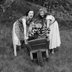 Two girls rolling two small boys down the hill in a wheelbarrow on a pleasant Spring day Two girls rolling two small boys down the hill in a wheelbarrow on a pleasant Spring day