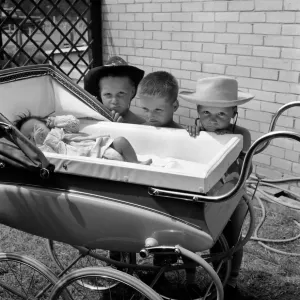 Three gloomy-faced triplet brothers aleaning over the side of a pram in the garden of