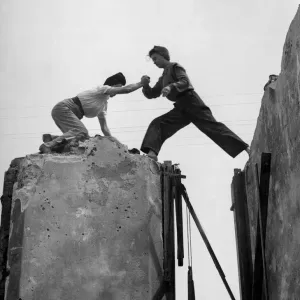 High up on the tottering wall, Lydia Walker steps across the gap aided by Betty Baker
