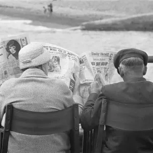 Holiday scenes at Brighton. Elderly couple reading the Daily Herald on Brighton Holiday scenes at Brighton. Elderly couple reading the Daily Herald on Brighton
