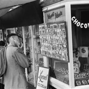 Urlaubsszenen in Hastings, Urlauber liest auf sinnlose Postkarten im Zigarettenladen Urlaubsszenen in Hastings, Urlauber liest auf sinnlose Postkarten im Zigarettenladen