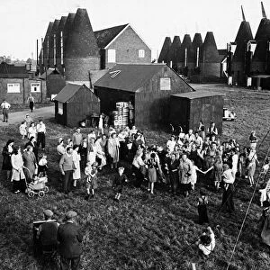 Hop pickers gathered in a Kent village with oast houses in the background, circa 1930
