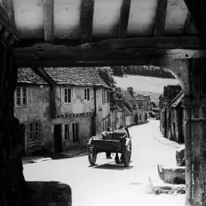 Horse drawn cart makes its way down a typical Cotswold village road in Gloucestershire Horse drawn cart makes its way down a typical Cotswold village road in Gloucestershire