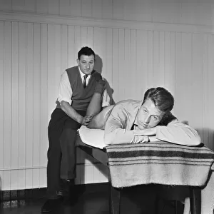 Injured Liverpool halfback Gordon Milne receives treatment on his thigh from team trainer