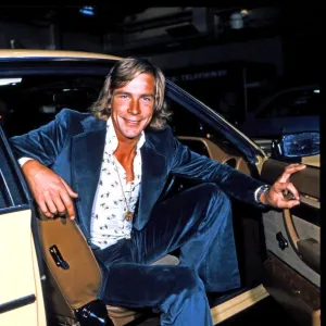 James Hunt, sourit à la caméra, alors qu'il est assis dans le siège avant de sa voiture.