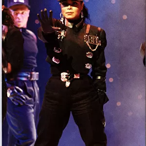 Janet Jackson on stage right arm outstretched wearing baseball cap performing