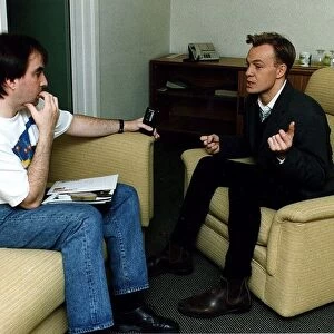Jason Donovan being interviewed black jeans jacket sitting in armchair ankle boots