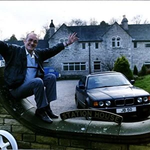 Jim Bowen comedian / TV presenter sitting on his garden wall with arms outstretched