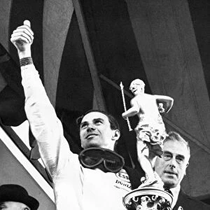 Jim Clark waves to the crowd as he holds the trophy presented to him by Earl Mountbatten