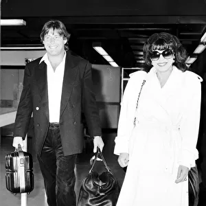 Joan Collins actress with boyfriend Bill Wiggins arriving at Heathrow Airport April