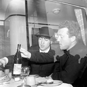 John Lennon wearing a bowler hat and smoking a cigarette at a dining table on the train