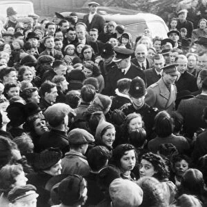 King George VI surrounded by a crowd of enthusiastic people welcoming him to the bomb
