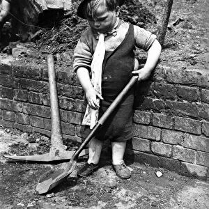 A little boy pays with a shovel following air raid attacks in England. Circa 1941