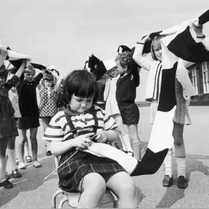 Little Wendy Scorer knits busily away. Her friends look on as a long scarf grows even