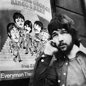 Liverpool playwright Willy Russell poses besides a poster for his play John, Paul, George