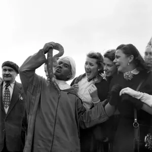 Local man of Morocco holding up a large snake near his mouth to the amusement of a group