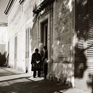 Two local men talking on the street in Italy - shadows casts circa 1950