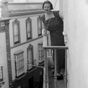 A local woman of Seville, Spain looks out over the town from the balcony of her town