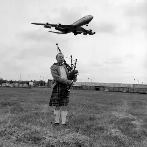 Lone bagpipe player Jim Thomas playing as a jumbo jet flies overhead May 1975
