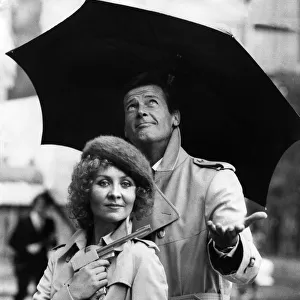 Lulu holding a Dunhill gun and Roger Moore together in the rain outside the Hilton Hotel
